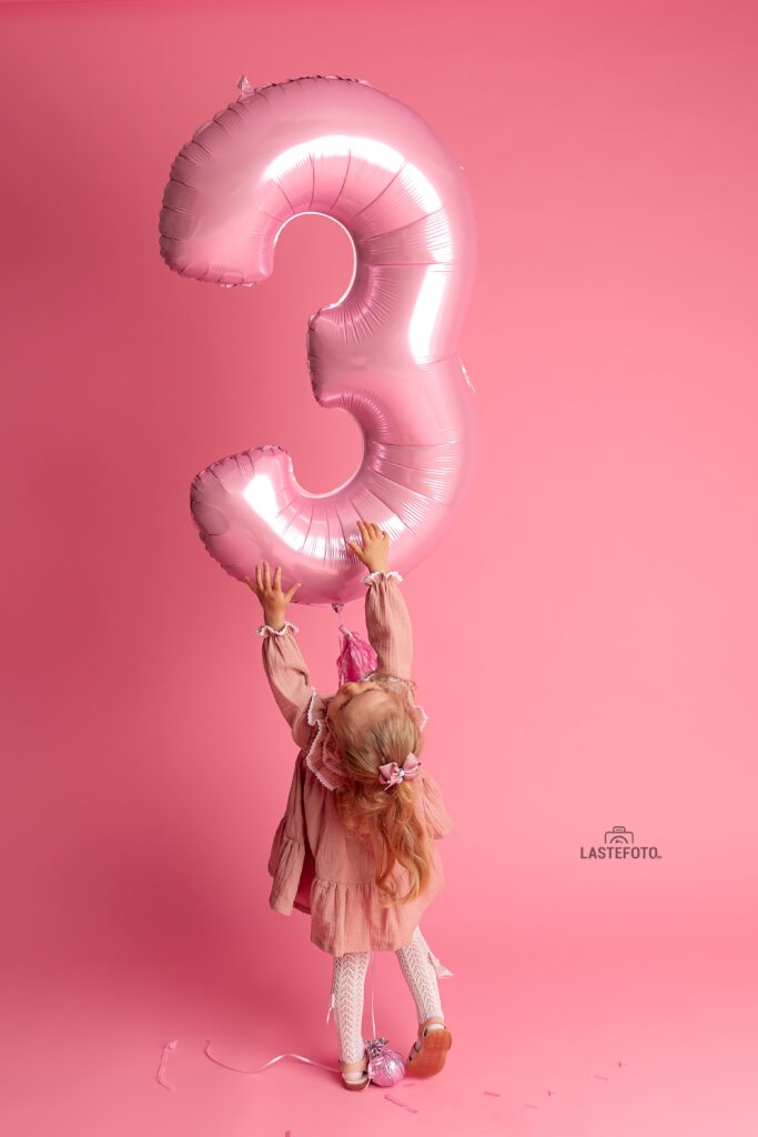 Väike tüdruk roosas kleidis tõstab roosa õhupalli numbriga kolm.