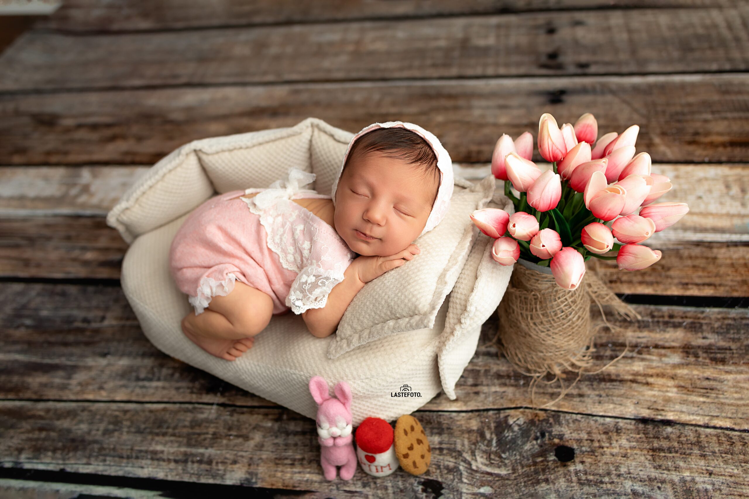 Why Is My Newborn Crying? 5 Surprising Reasons and What You Can Do About It 1 Newborn baby sleeping in a pink lace outfit on a small cushion, with tulips and soft toys nearby.