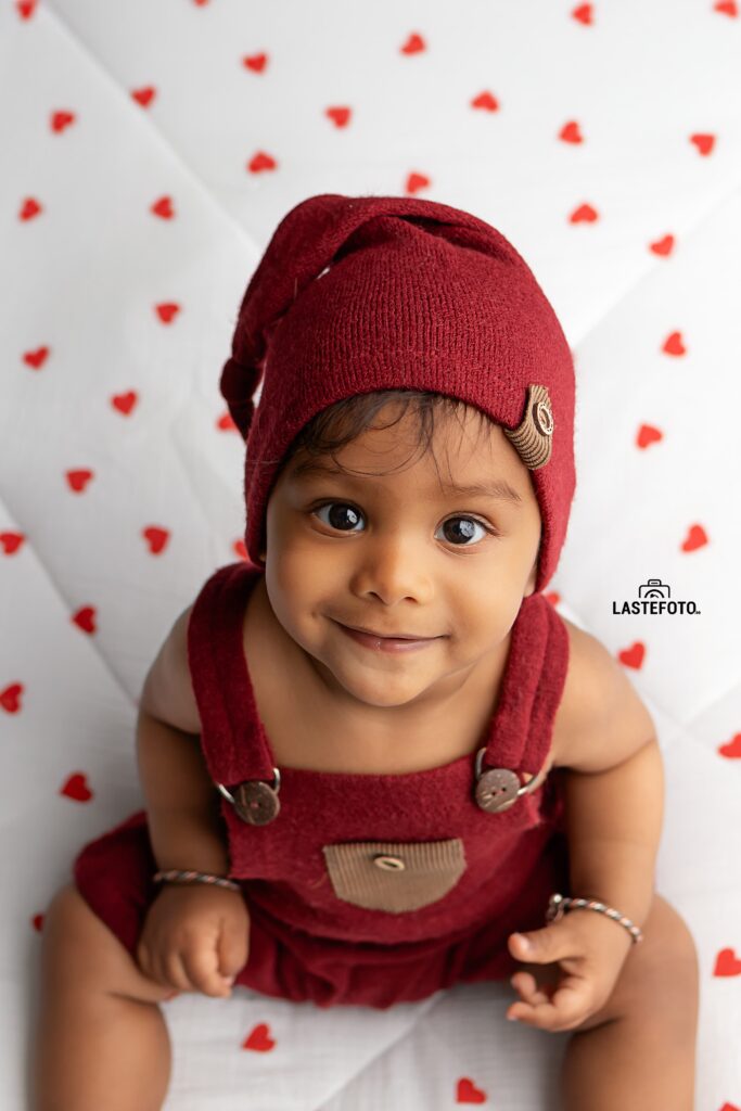 Early Childhood Development: Essential for the Child or Peace of Mind for the Mother? 2 Smiling baby in red romper and hat on a white background with hearts – early childhood development in Tallinn