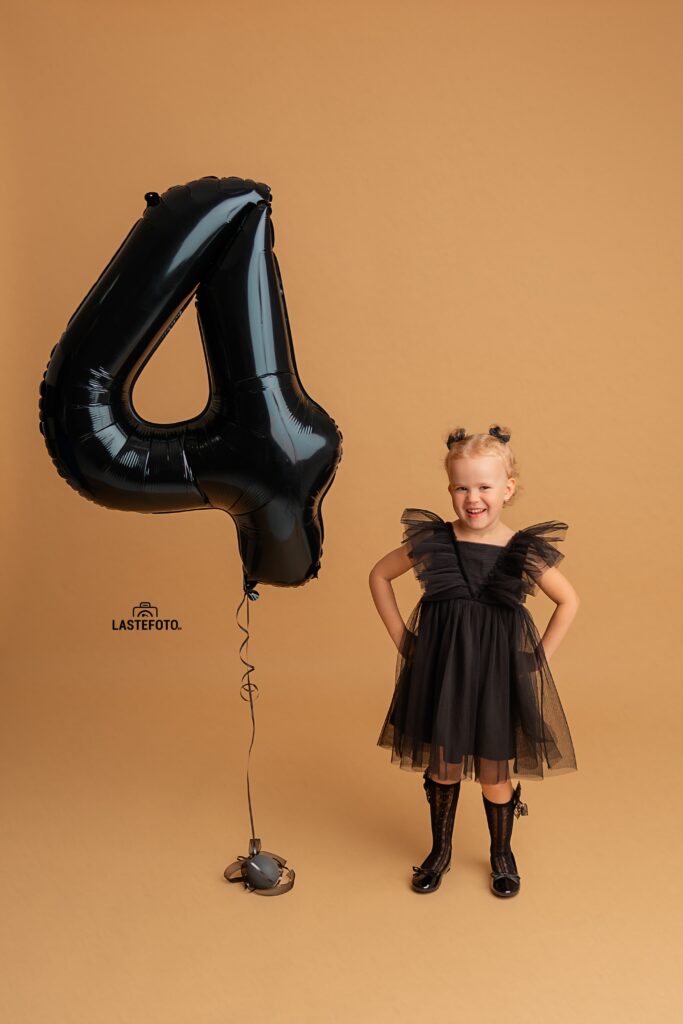 Kids Birthday Photoshoot in Studio – Why Capturing Every Age Matters 5 kids birthday photoshoot in studio – girl in a black tulle dress with hands on hips; large black number 4 balloon on a beige background