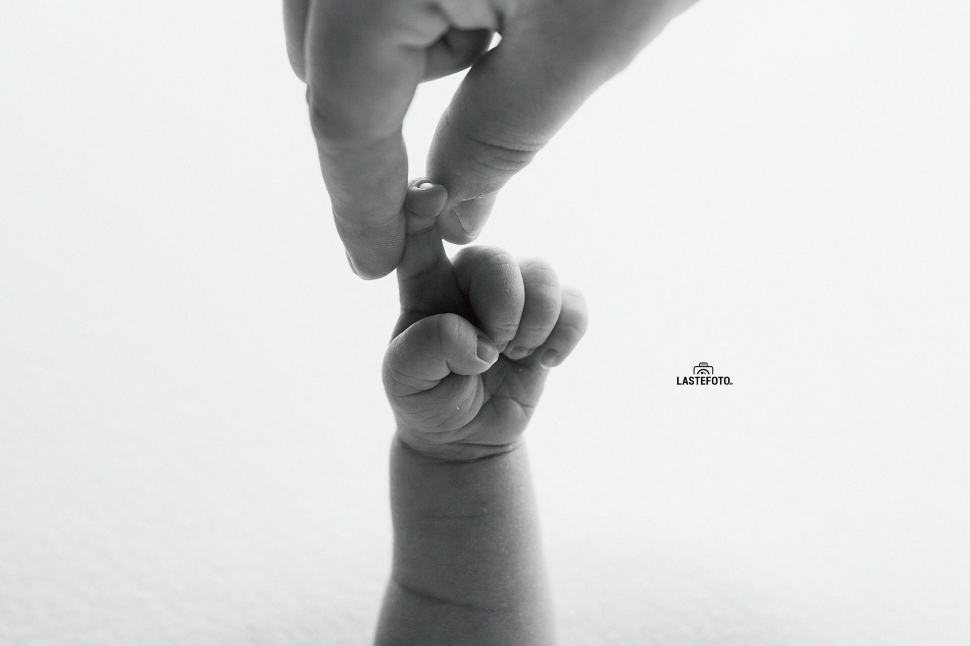 newborn hand gently holding an adult finger in a black and white photo