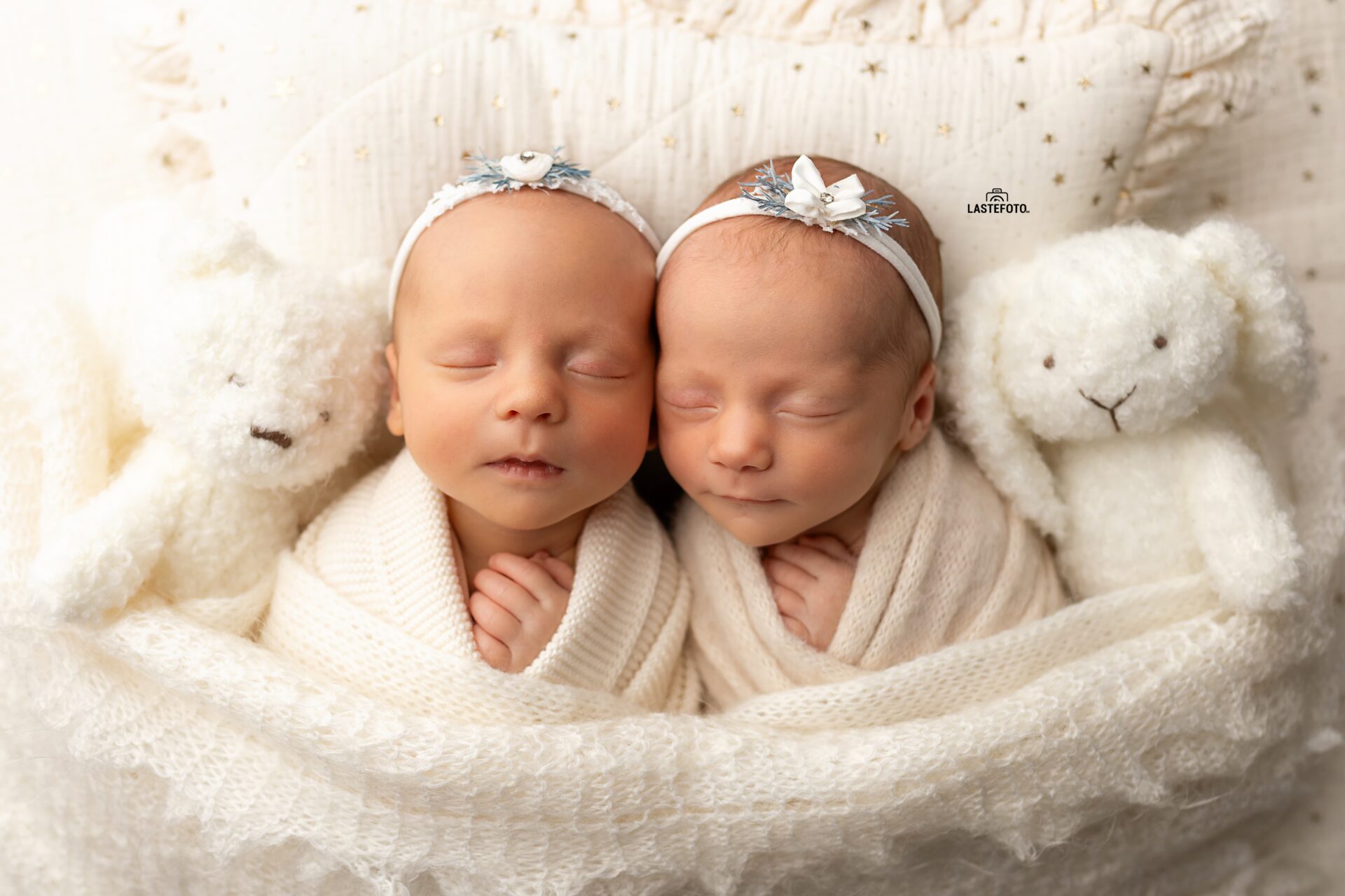 Newborn Twins Photoshoot: two sleeping twin girls in white headbands, swaddled together between a teddy bear and a bunny