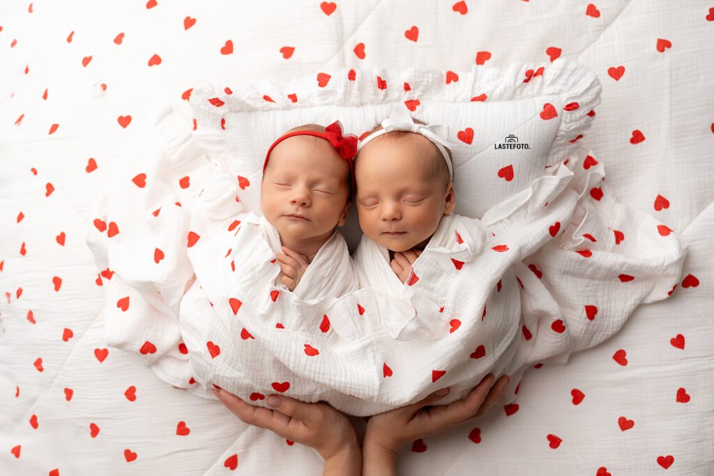 Newborn Twins Photoshoot: 6 Practical Tips for Calm, Confident Planning and Preparation 2 Newborn Twins Photoshoot: two sleeping twin girls in white heart-patterned wraps with headbands, supported by parents’ hands