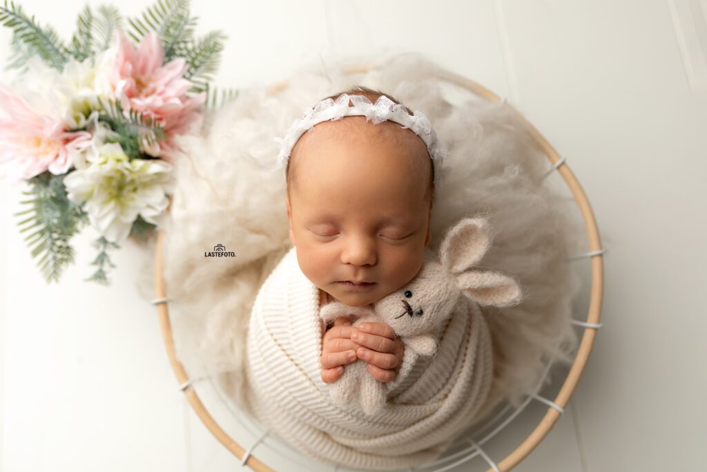 Newborn Twins Photoshoot: 6 Practical Tips for Calm, Confident Planning and Preparation 3 Newborn Twins Photoshoot: sleeping baby girl in a white lace headband, swaddled in cream knit, holding a tiny knitted bunny in a round basket with soft wool and pastel flowers