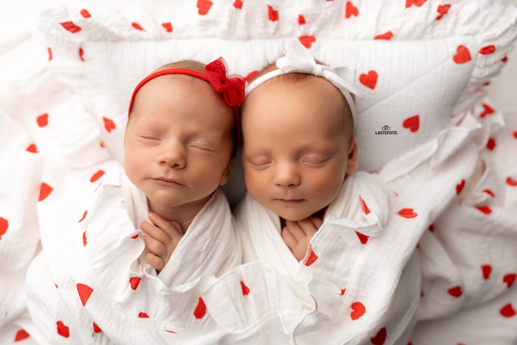 Newborn Twins Photoshoot: 6 Practical Tips for Calm, Confident Planning and Preparation 5 Newborn Twins Photoshoot: two sleeping twin girls in white wraps with red hearts, headbands with red and white bows, close-up