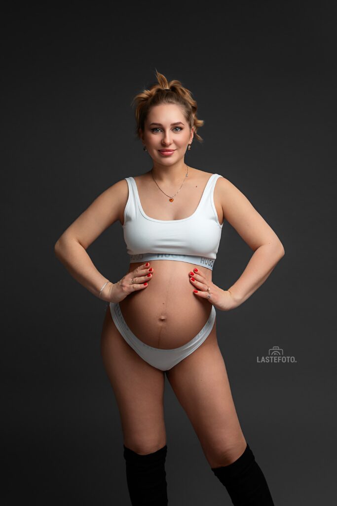 When to Do a Maternity Photoshoot: The Best Timing and 7 Things Most People Don’t Talk About 3 Studio portrait of a pregnant woman in light underwear on a dark background, highlighting the shape of the belly and confident pose