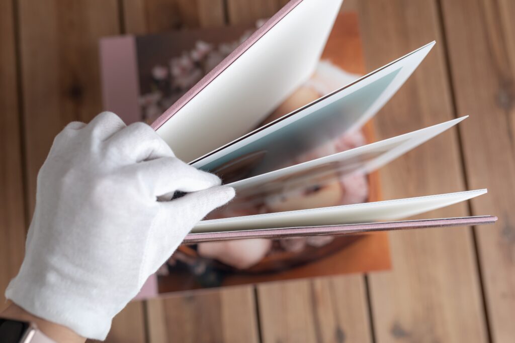 Photobook With Your Heartwarming Family Story - Made to Be Opened Again and Again 4 Photobook with thick pages and a pink cover, carefully opened with white gloves on a wooden background.